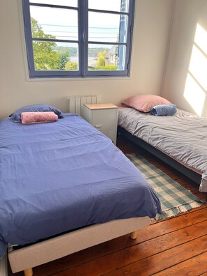 Un dormitorio con dos camas, un radiador, un armario pequeño y vistas a la vegetación a través de una ventana.