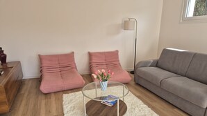 A living room with a grey sofa, two pink poufs, a glass coffee table with a book, and a vase with flowers.
