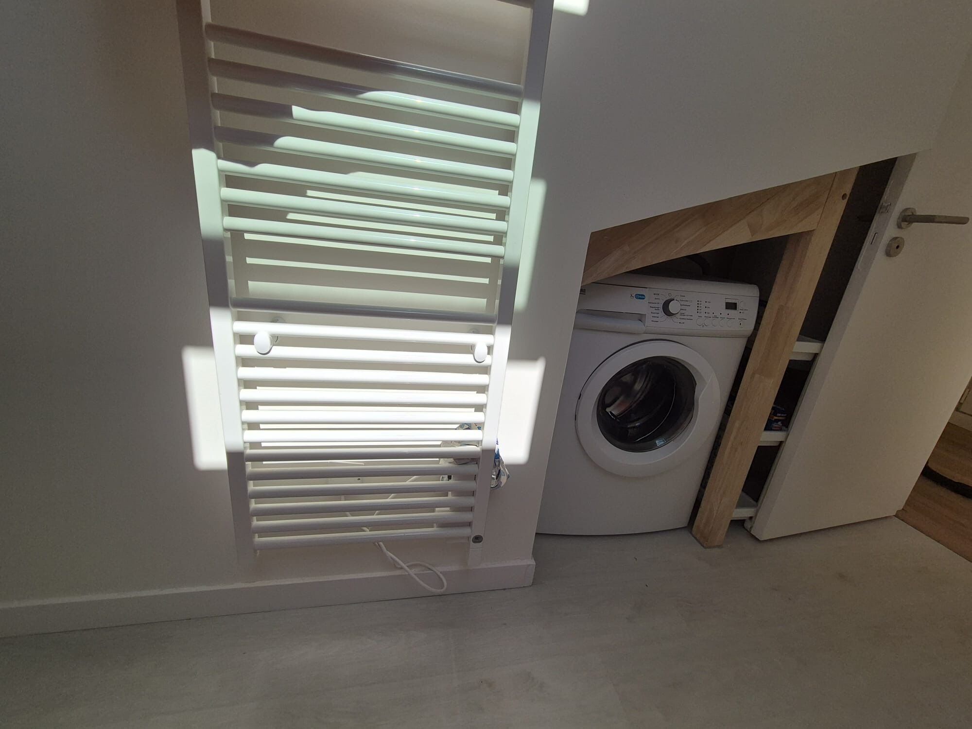 A laundry room with a washing machine and a dryer, a wooden cabinet, and a door with horizontal blinds.