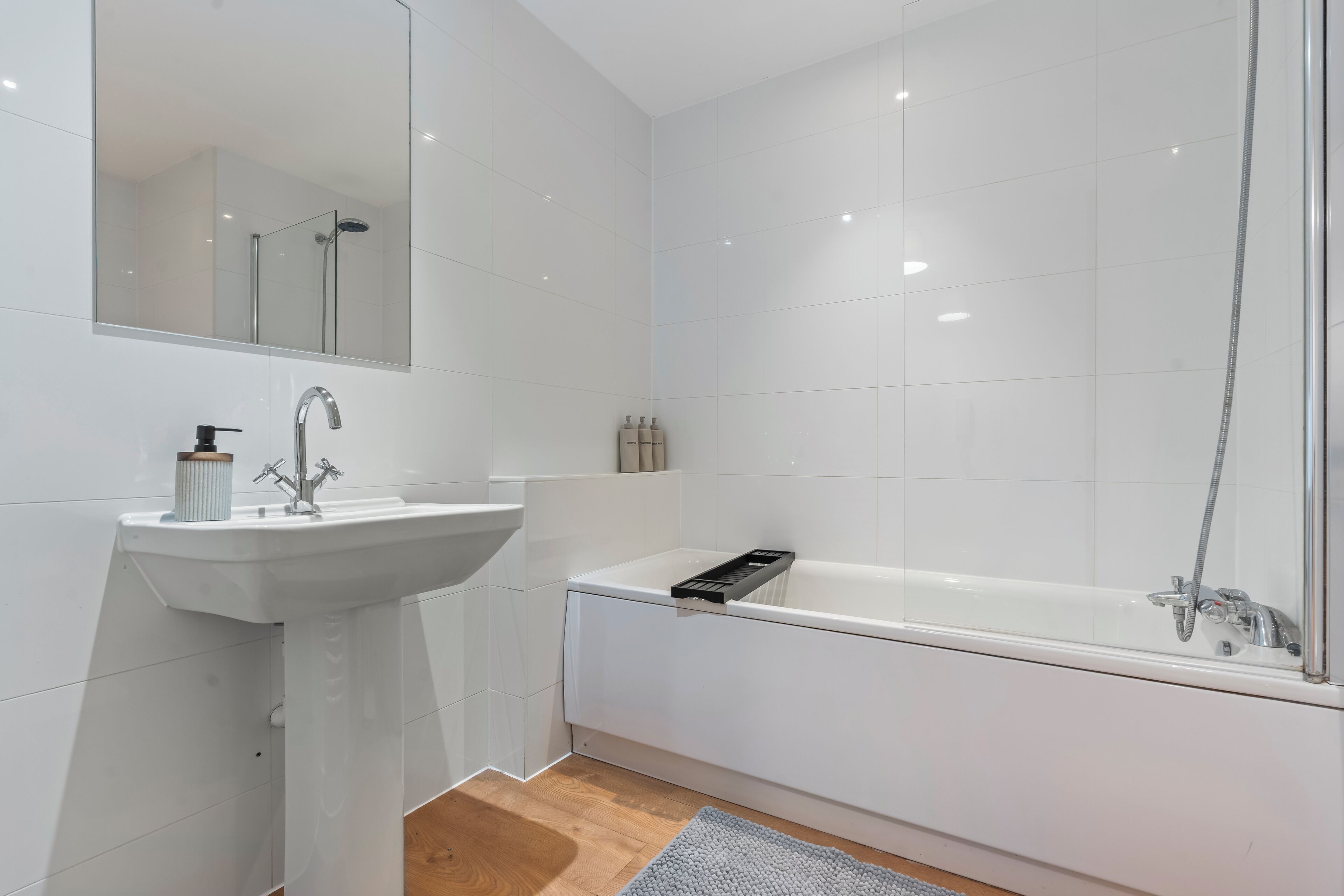 A modern bathroom with a white sink, mirror, and bathtub.