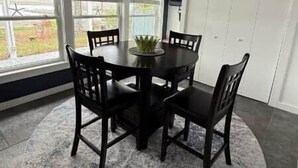 Un coin repas comprenant une table ronde, quatre chaises, un ventilateur de plafond et de grandes fenêtres.