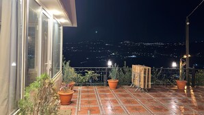 A terrace with potted plants, a tiled floor, and a view of a cityscape at night. - Secluded Hilltop Villa Near Ancient Jarash — Privacy, Views & Pure Tranquility (Jerash)