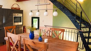 Un coin repas avec une table en bois, des chaises, un vase de fleurs et un escalier.