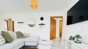 A modern living room with a sofa, two round tables, a TV, and a minimalist decor. - 3 BEDROOMS AND TWO BATHROOMS, CLOSE TO DOWNTOWN, WITH 2 SWIMMING POOLS IN THE COMMON AREA. (Punta Cana)