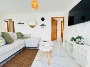 Ein modernes Wohnzimmer mit einer Couch, zwei runden Tischen, einem Fernseher und einer minimalistischen Einrichtung.