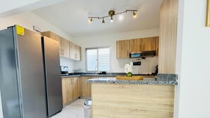A modern kitchen with stainless steel appliances, wooden cabinets, and a granite countertop. - 3 BEDROOMS AND TWO BATHROOMS, CLOSE TO DOWNTOWN, WITH 2 SWIMMING POOLS IN THE COMMON AREA. (Punta Cana)