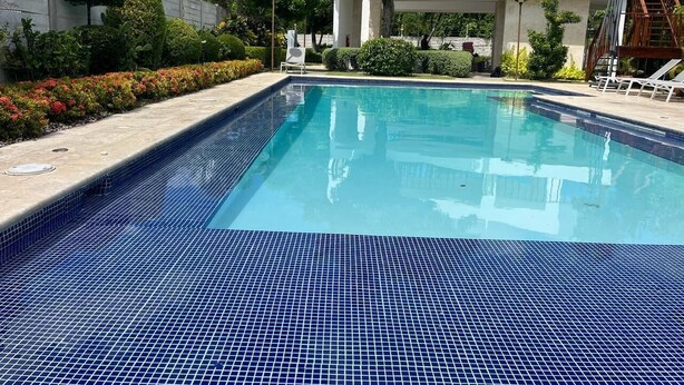 A rectangular swimming pool with blue tiles, surrounded by a concrete deck and a low wall. - 3 BEDROOMS AND TWO BATHROOMS, CLOSE TO DOWNTOWN, WITH 2 SWIMMING POOLS IN THE COMMON AREA. (Punta Cana)