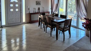 A spacious dining area with a large table and chairs, a ceiling fan, and a view of the outdoors through large windows.