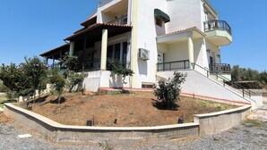 A modern two-story house with a balcony, a covered patio, and a landscaped garden area.