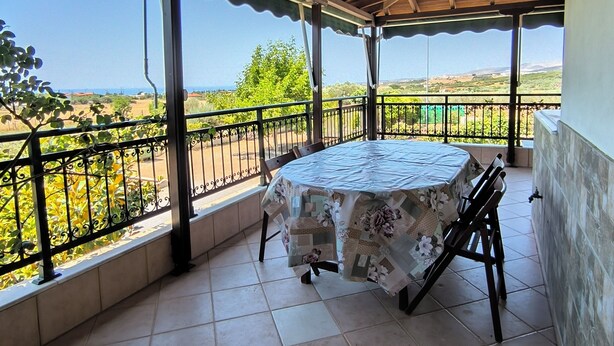 A covered patio with a table and chairs, a view of the landscape, and a tiled floor.