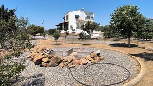 A residential building with a white facade, a balcony, and a landscaped garden with a circular gravel area and rocks.