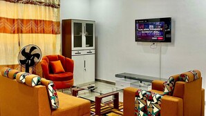 A modern living room with two sofas, a glass coffee table, a cabinet, a television, and a patterned curtain.