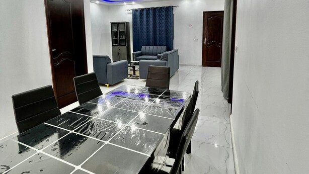 A modern conference room with a glass-top table, black chairs, a dark wooden cabinet, and a blue curtain.