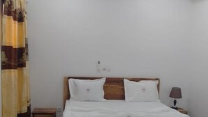 A bedroom with a wooden bed, white bedding, a nightstand, a lamp, and a ceiling light fixture.