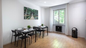 Un comedor con una mesa dispuesta para cuatro personas, un radiador y una ventana con cortinas.
