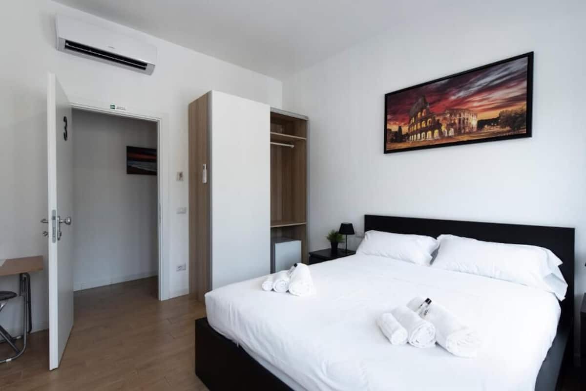 Una habitación de hotel con cama, un cuadro, un armario y un equipo de aire acondicionado.