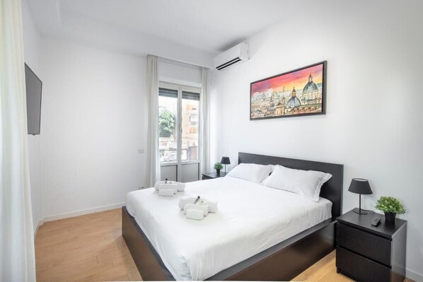 A hotel room with a bed, a nightstand, a painting, and a window.