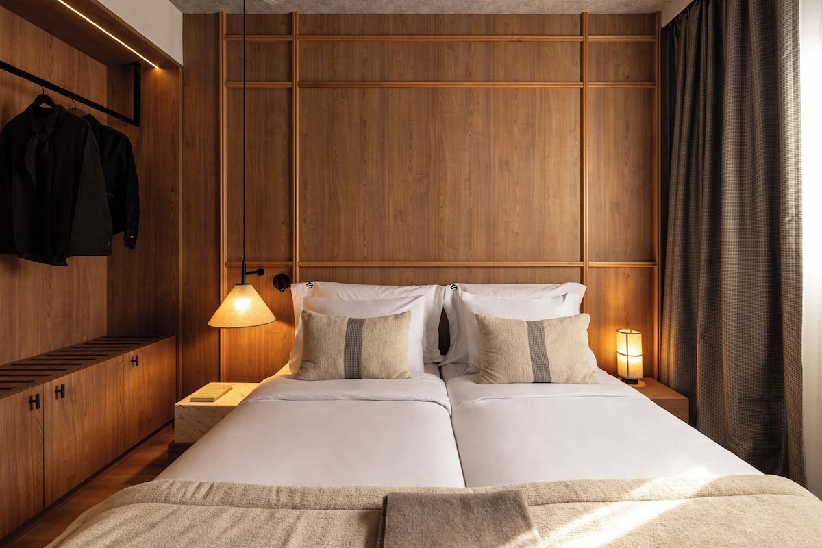 A double bed with a wooden headboard, two bedside lamps, and a hanging coat rack.