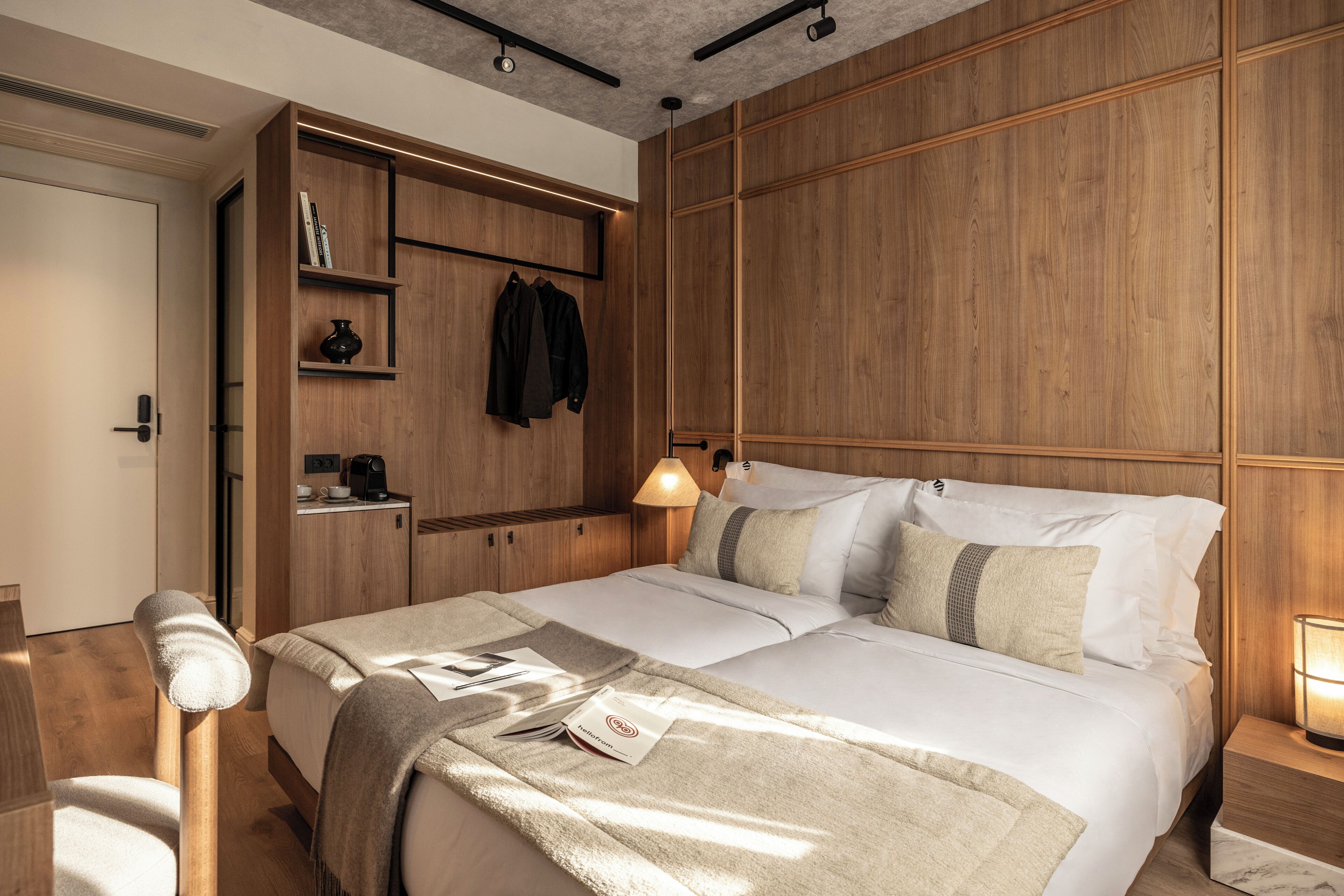 A modern bedroom with a wooden headboard, a bedside table with a lamp, and a bed with a white comforter.
