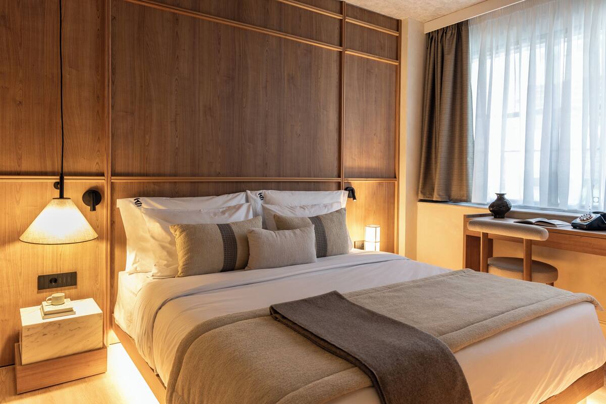 A hotel room with a large bed, bedside lamps, a nightstand, and a window with curtains.