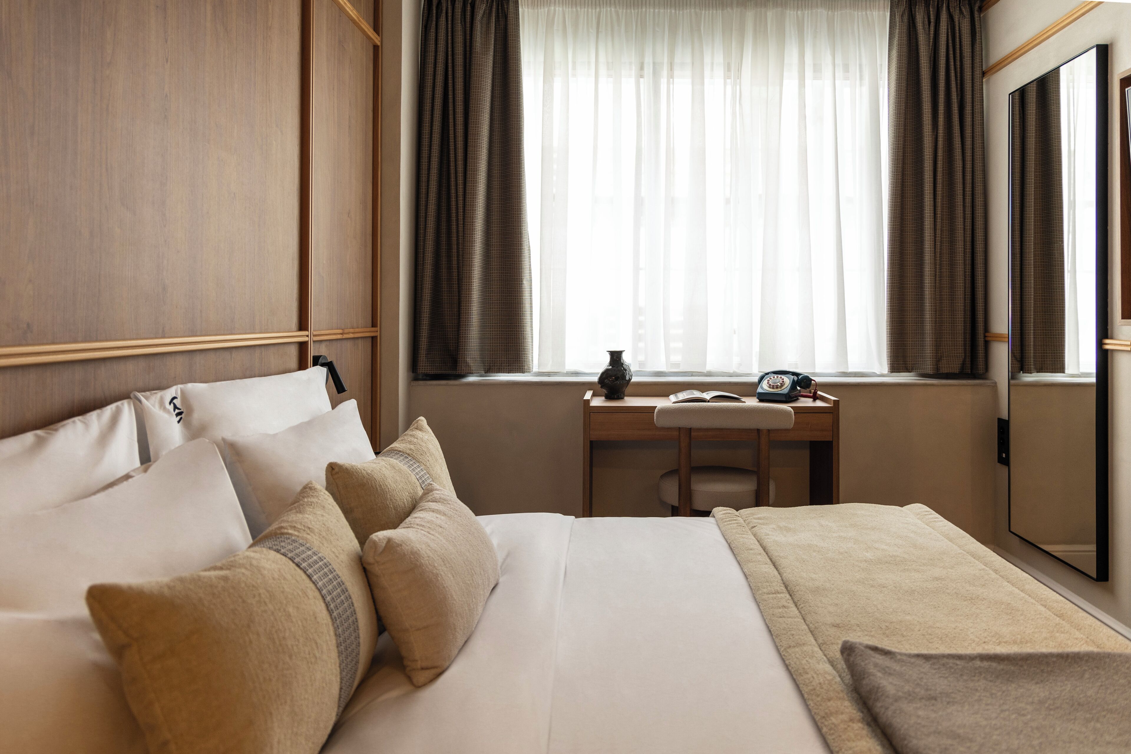 A hotel room with a bed, a desk, a chair, a telephone, and a mirror.