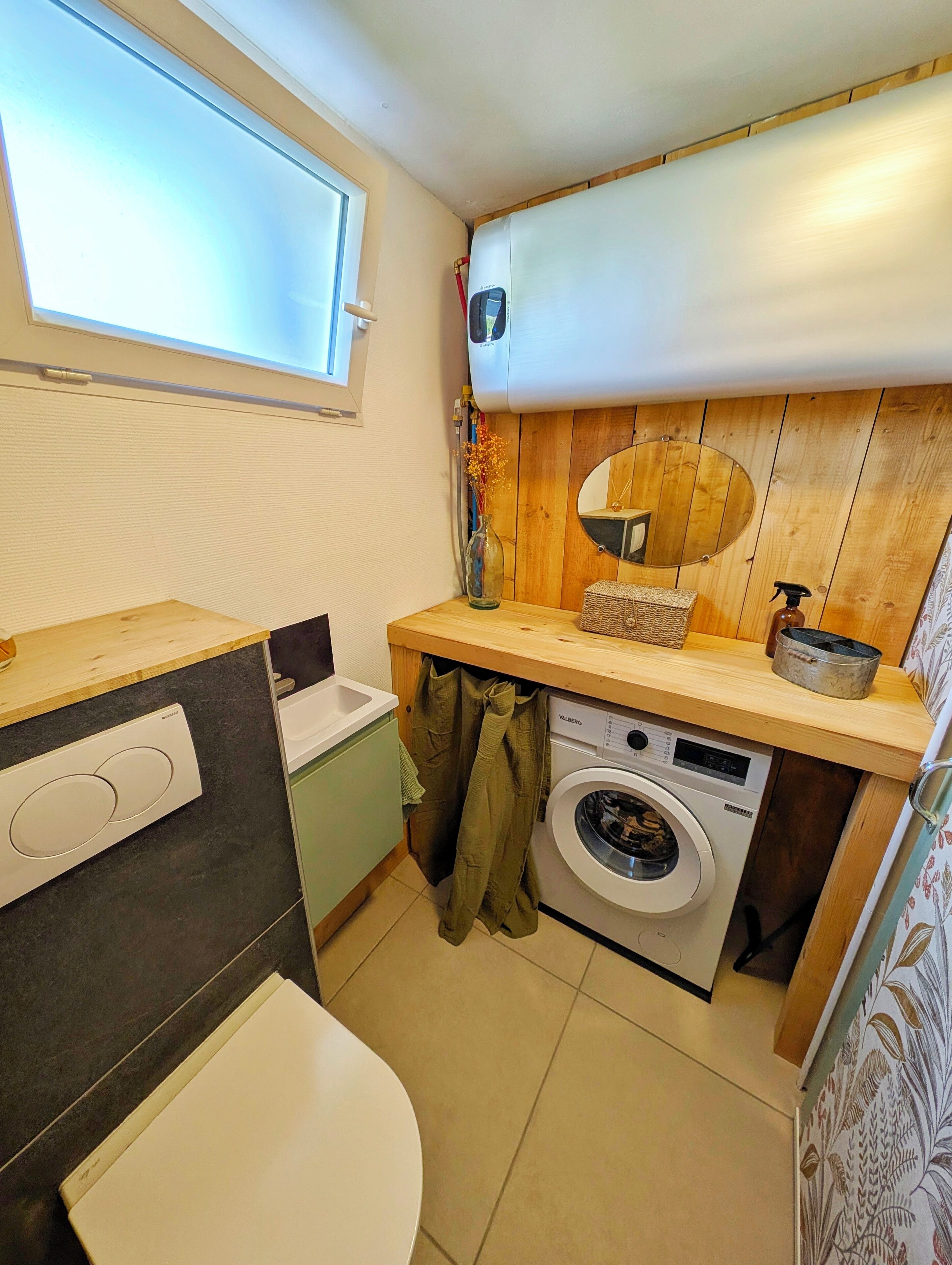 A compact kitchen with a built-in washing machine, a window, and a wooden wall panel.