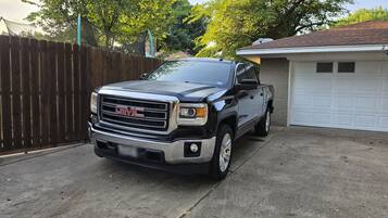 A GMC truck parked in a driveway with a garage and a wooden fence in the background.
