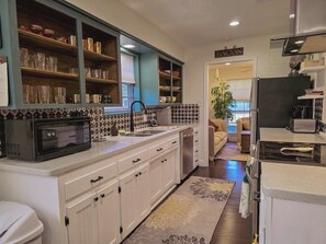 A kitchen with white cabinets, a microwave, a sink, and a refrigerator. - Vintage McKinney • Spacious '70s Ranch, Hot Tub • 8 min to Downtown (McKinney)