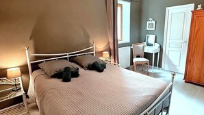 Ein Schlafzimmer mit einem Bett, Nachttischen, einem Sessel, einem Schreibtisch und einem Kleiderschrank.