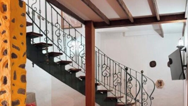 Ein Essbereich mit Holztisch und Stühlen, einer Treppe mit schmiedeeisernen Geländern und einem gemusterten Teppich auf dem Boden.