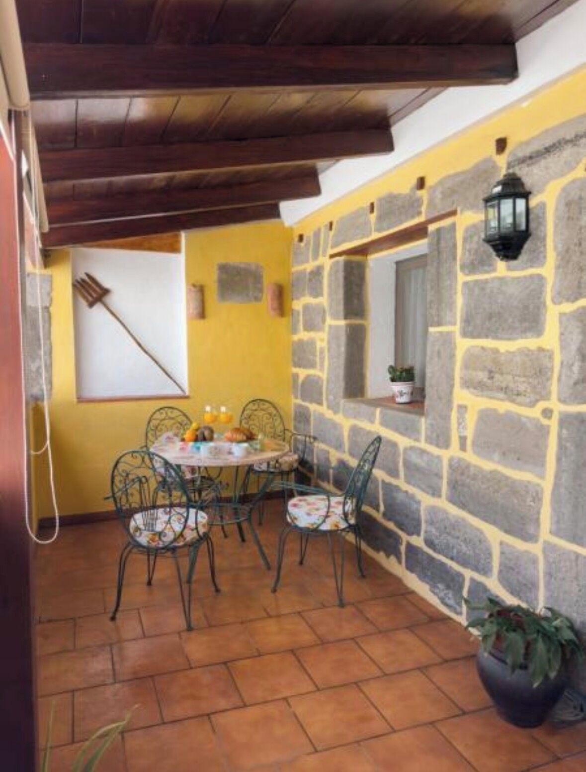 A patio with a stone wall, a table with chairs, a hanging lantern, and a potted plant.