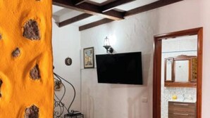 Ein Zimmer mit Holzboden, einem an der Wand montierten Fernseher, einem kleinen Tisch mit Lampe und einer Tür zu einem anderen Raum.