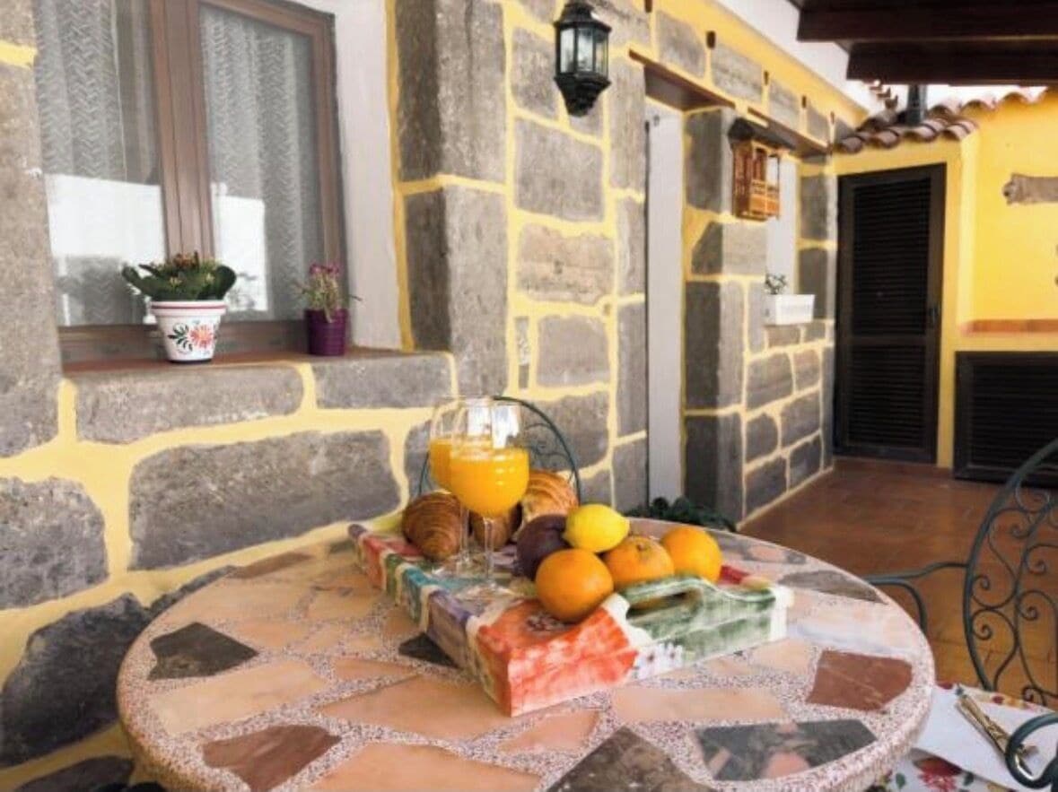Een gebouw van steen met een betegeld terras, een tafel met eten en drinken, en een raam met planten.