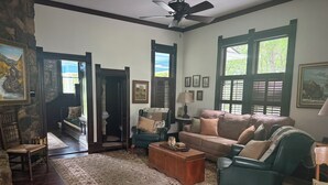 Uma sala de estar com lareira, uma poltrona verde, um sofá, uma mesa de centro e um tapete.