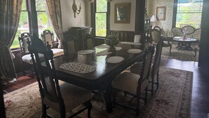 Uma sala de jantar formal com mesa de madeira, cadeiras, toalhas de renda e um candelabro.