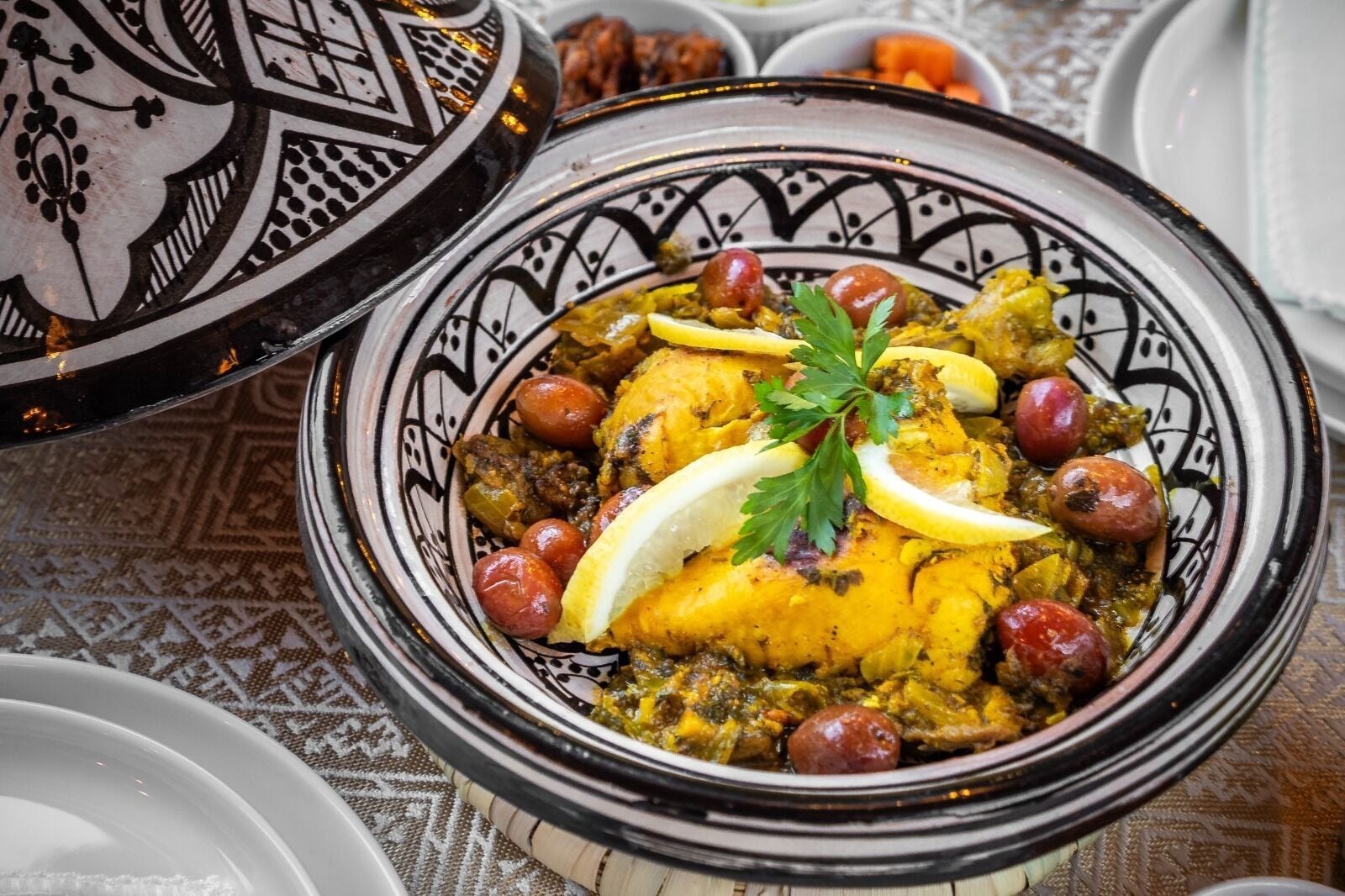 Ein traditionelles marokkanisches Tajine-Gericht mit dekorativem Deckel, garniert mit Petersilie und Zitronenscheiben.