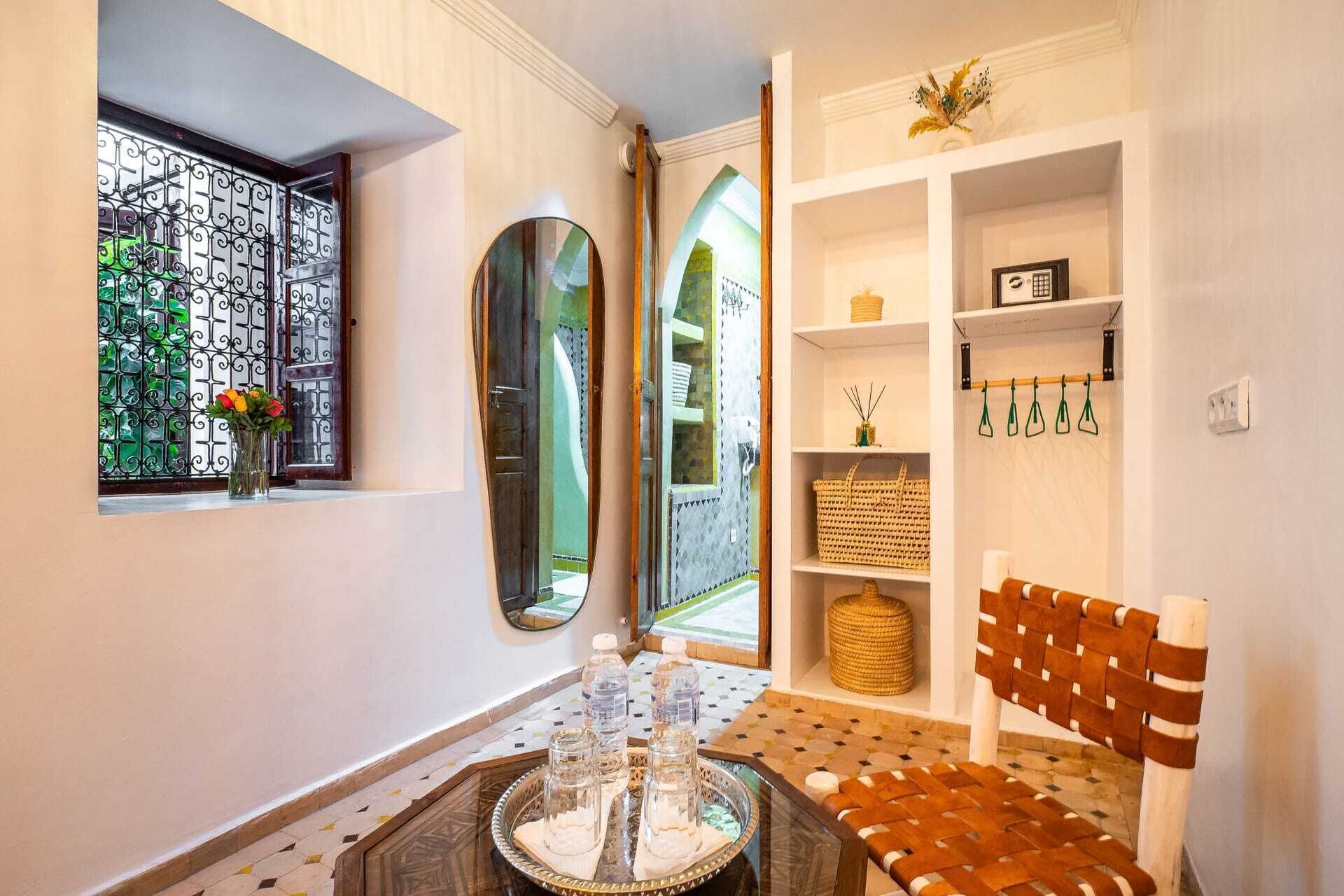 A hallway with a glass door, a mirror, a seating area with a woven chair, and a shelf with decorative items.