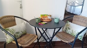 Ein kleiner runder Tisch mit Korbstühlen, einem Brotkorb, einer Marmeladenglas und einer grünen Tasse.