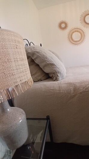 Ein Bett mit einer beigen Decke und Kissen, eine gewebte Lampe und eine Wand mit runder Dekoration.