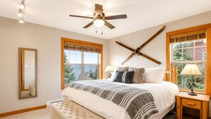 A bedroom with a bed, a ceiling fan, a window with a view, a bedside table, and a nightstand.