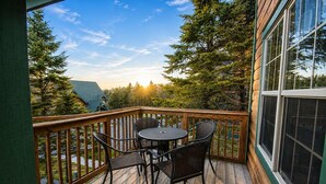 A wooden deck with a table and chairs, surrounded by trees and a view of the landscape.