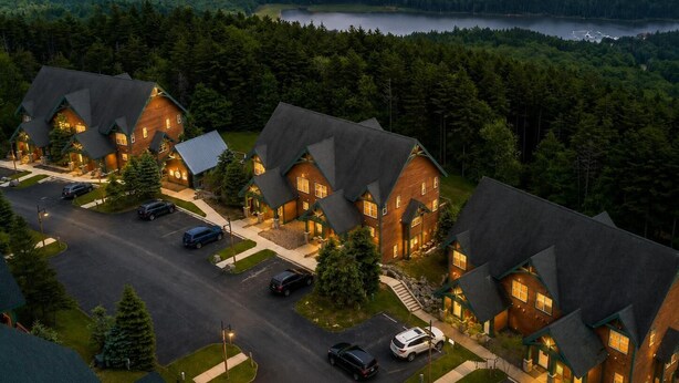 A cluster of log cabin-style houses with a lake and forested hills in the background.