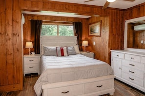 Quarto com painéis de madeira, cama, mesas de cabeceira, cômoda e ventilador de teto.