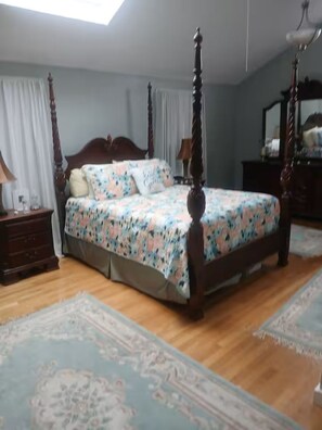 A bedroom with a four-poster bed, a nightstand, a dresser, and a mirror.