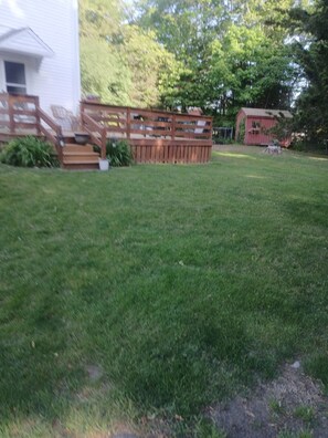 A grassy yard with a wooden deck and a red shed.