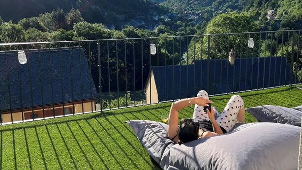Une personne allongée sur une terrasse recouverte d’herbe, avec vue sur une vallée et des collines.