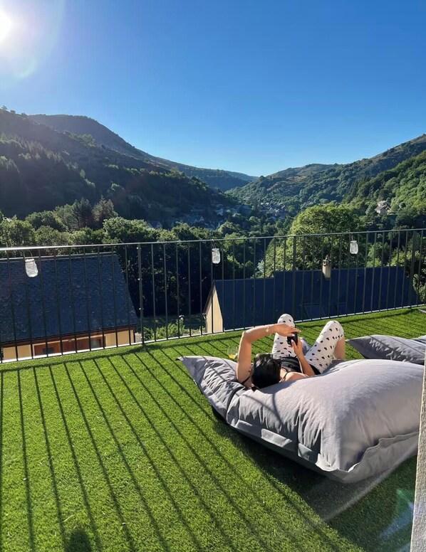 Eine Person liegt auf einer mit Gras bedeckten Terrasse mit Blick auf ein Tal und Hügel.