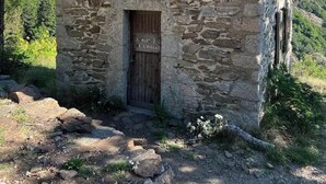 Un bâtiment en pierre avec une porte en bois et une petite fenêtre, entouré de verdure et sous un ciel dégagé.
