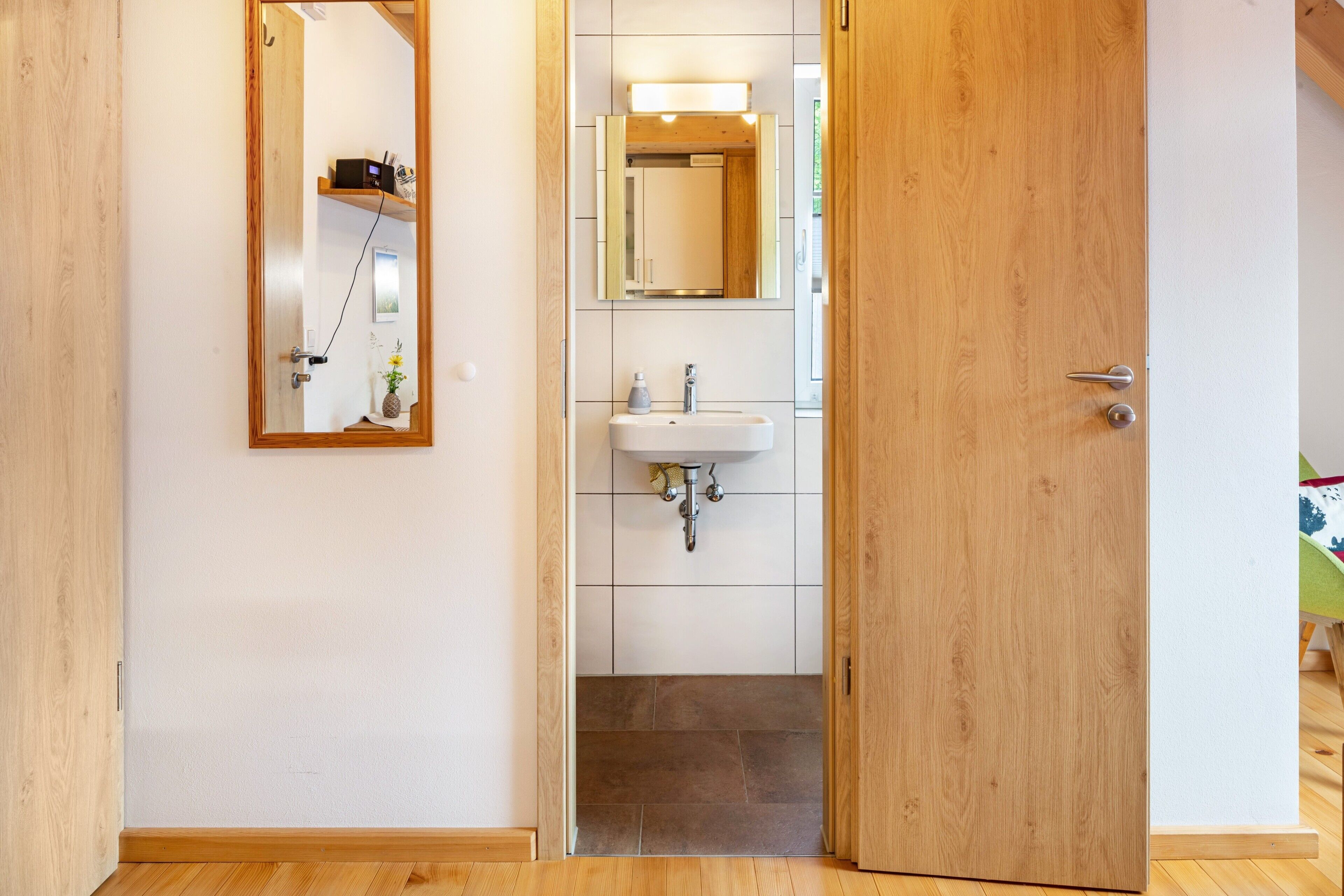 A wooden door leading to a bathroom with a white sink, a mirror, and a shelf with a radio.