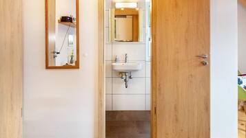 A wooden door leading to a bathroom with a white sink, a mirror, and a shelf with a radio.